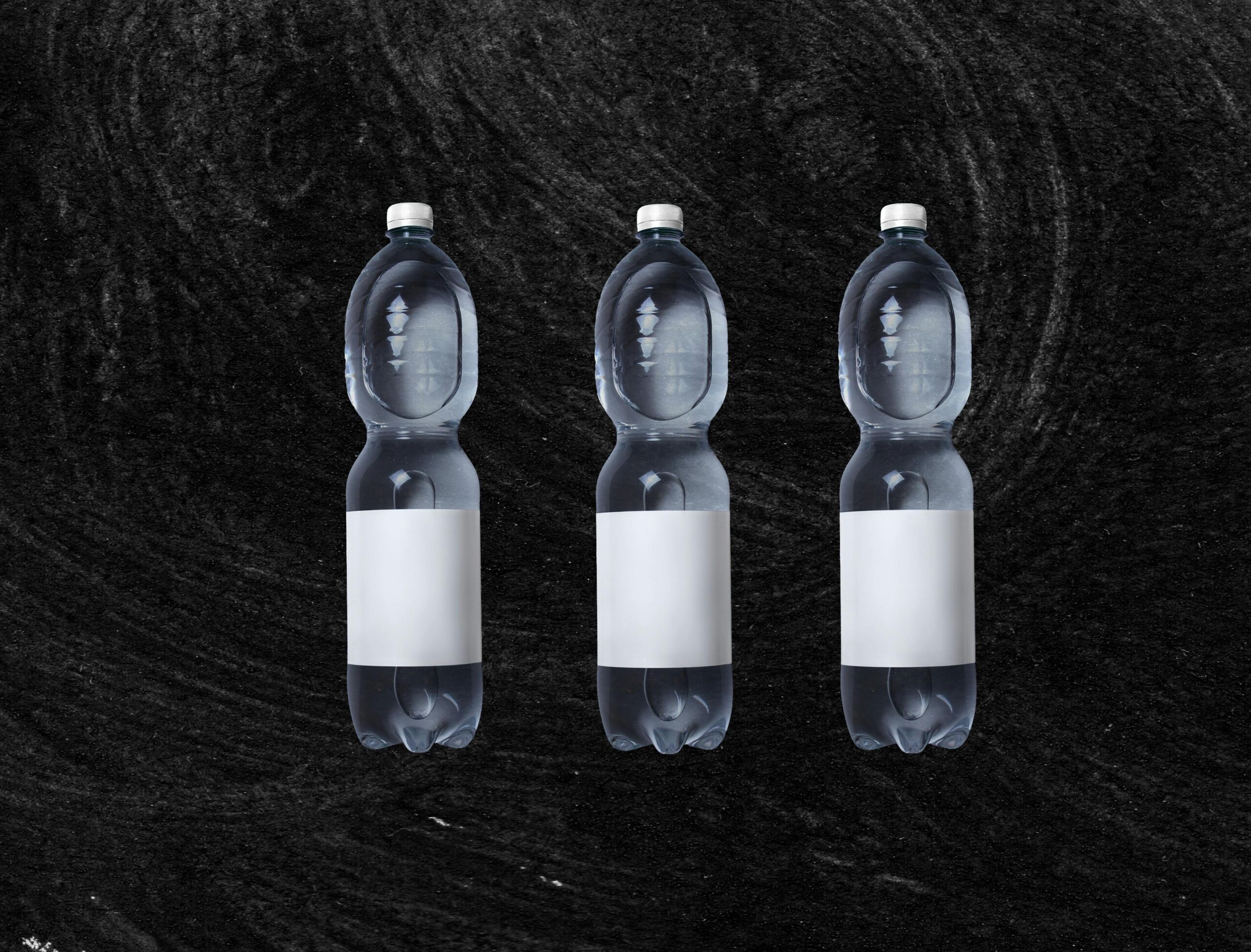 A set of three clear plastic water bottles on a textured black background, offering ample copy space.